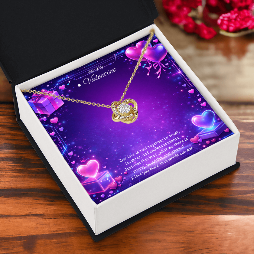 Gold love knot necklace with a sparkling center stone displayed on a purple Valentine’s Day background with glowing hearts, symbolizing eternal love and romantic connection.