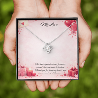 Silver love knot necklace with a sparkling center stone displayed in a  gift box on a soft Valentine-themed background with hearts and romantic message card.