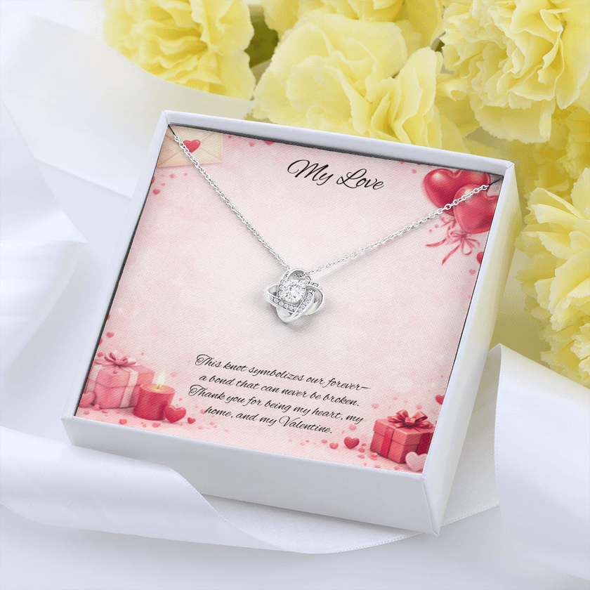 Silver love knot necklace with a sparkling center stone displayed in a  gift box on a soft Valentine-themed background with hearts and romantic message card.