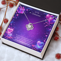Silver love knot necklace with a sparkling center stone displayed on a purple Valentine’s Day background with glowing hearts, symbolizing eternal love and romantic connection.
