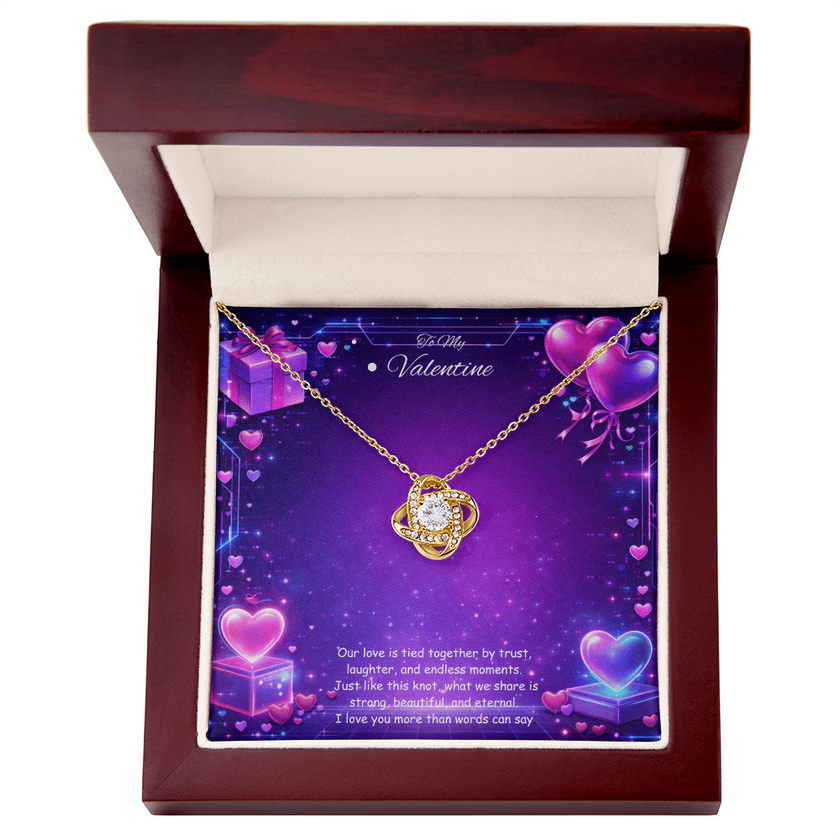 Gold love knot necklace with a sparkling center stone displayed on a purple Valentine’s Day background with glowing hearts, symbolizing eternal love and romantic connection.