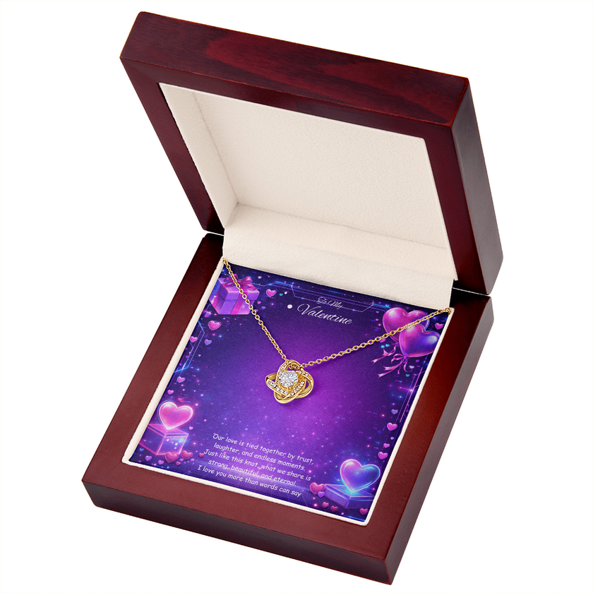 Gold love knot necklace with a sparkling center stone displayed on a purple Valentine’s Day background with glowing hearts, symbolizing eternal love and romantic connection.