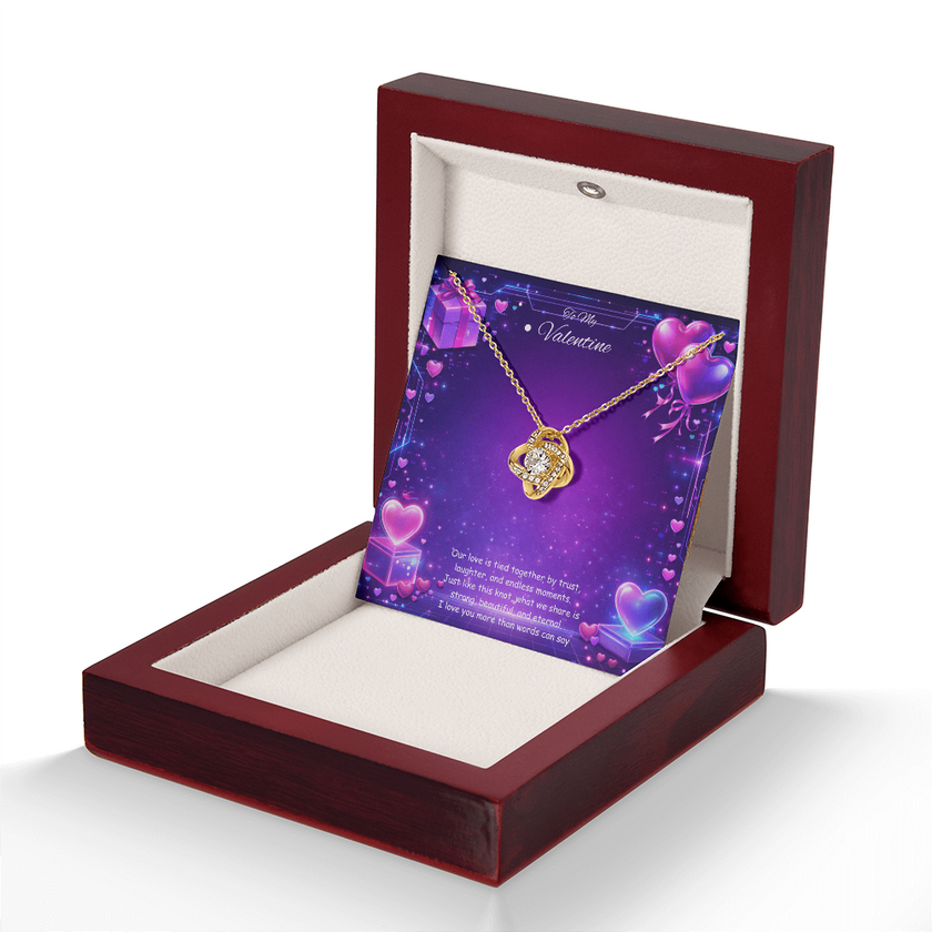 Gold love knot necklace with a sparkling center stone displayed on a purple Valentine’s Day background with glowing hearts, symbolizing eternal love and romantic connection.