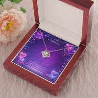 Silver love knot necklace with a sparkling center stone displayed on a purple Valentine’s Day background with glowing hearts, symbolizing eternal love and romantic connection.