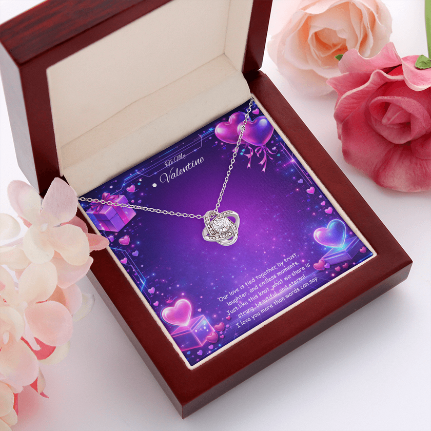 Silver love knot necklace with a sparkling center stone displayed on a purple Valentine’s Day background with glowing hearts, symbolizing eternal love and romantic connection.
