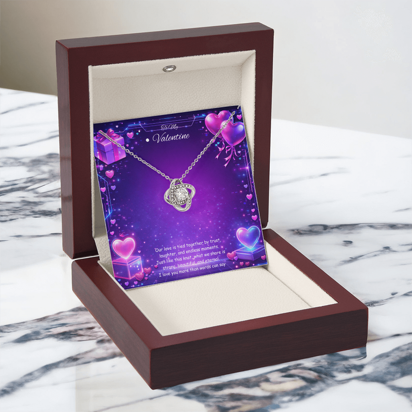 Silver love knot necklace with a sparkling center stone displayed on a purple Valentine’s Day background with glowing hearts, symbolizing eternal love and romantic connection.