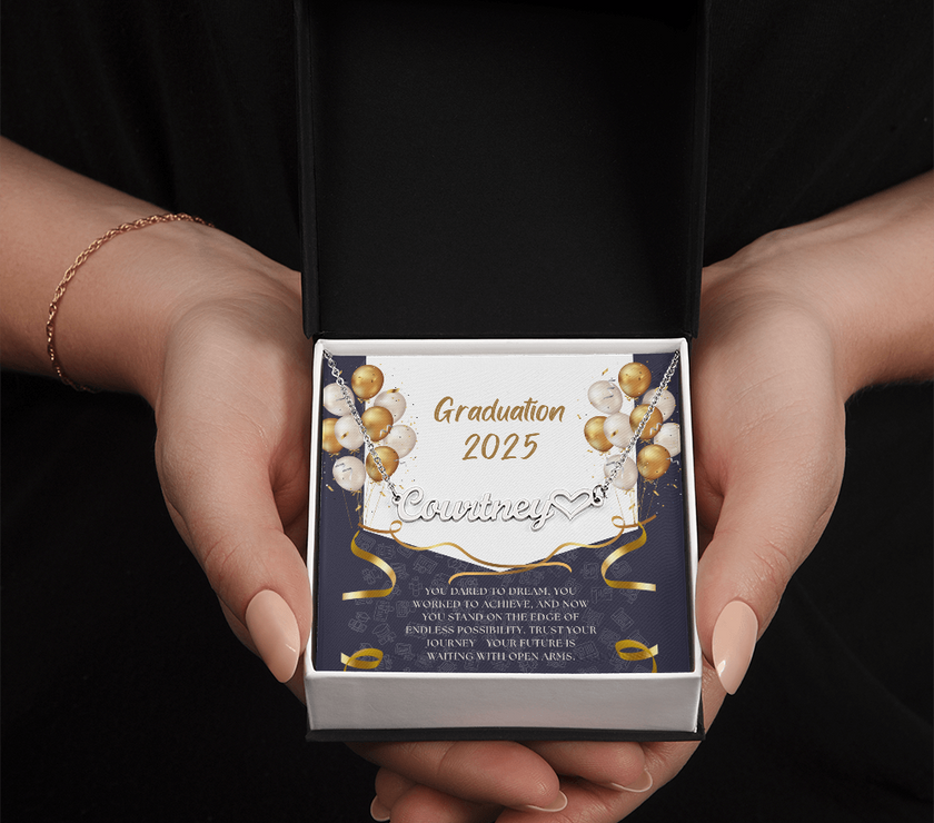Close-up of hands holding an open red gift box featuring a personalized silver name necklace with heart, set against a message card that reads "Graduation 2025" and includes an inspiring graduation quote, with gold and white balloons in the background.