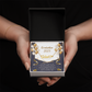 Close-up of hands holding a 
personalized gold name necklace with heart, set against a message card that reads "Graduation 2025" and includes an inspiring graduation quote, with gold and white balloons in the background.