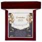 Close-up of hands holding an open red gift box featuring a personalized silver name necklace with heart, set against a message card that reads "Graduation 2025" and includes an inspiring graduation quote, with gold and white balloons in the background.