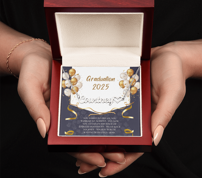 Close-up of hands holding an open red gift box featuring a personalized silver name necklace with heart, set against a message card that reads "Graduation 2025" and includes an inspiring graduation quote, with gold and white balloons in the background.