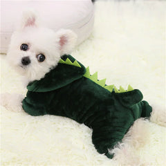 Small white dog wearing a green dinosaur costume on a white surface