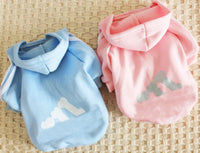 Blue and pink pet hoodies with paw print designs on a woven surface