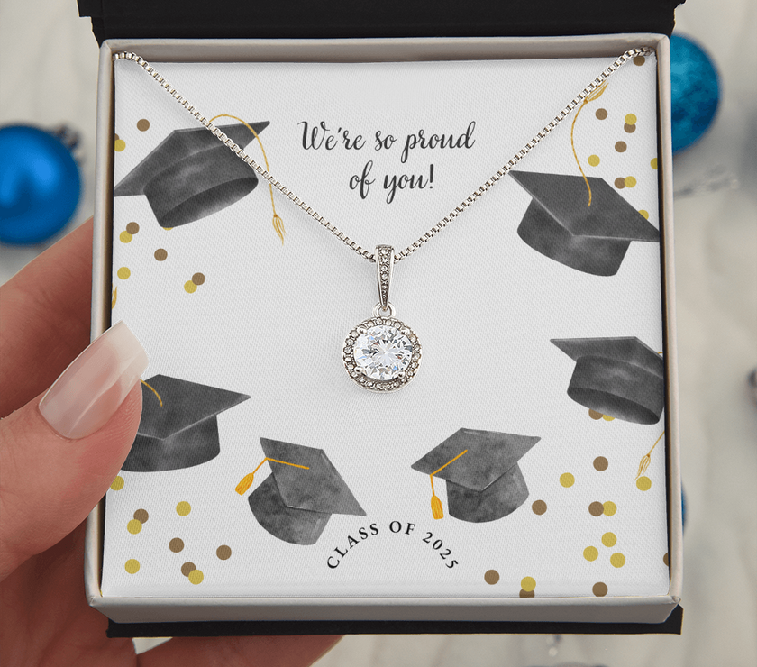 A hand holds an open gift box displaying a sparkling silver Eternal Hope necklace with a round pendant, set against a graduation-themed message card that reads "We're so proud of you!" with graduation caps, gold confetti, and "Class of 2025" text.