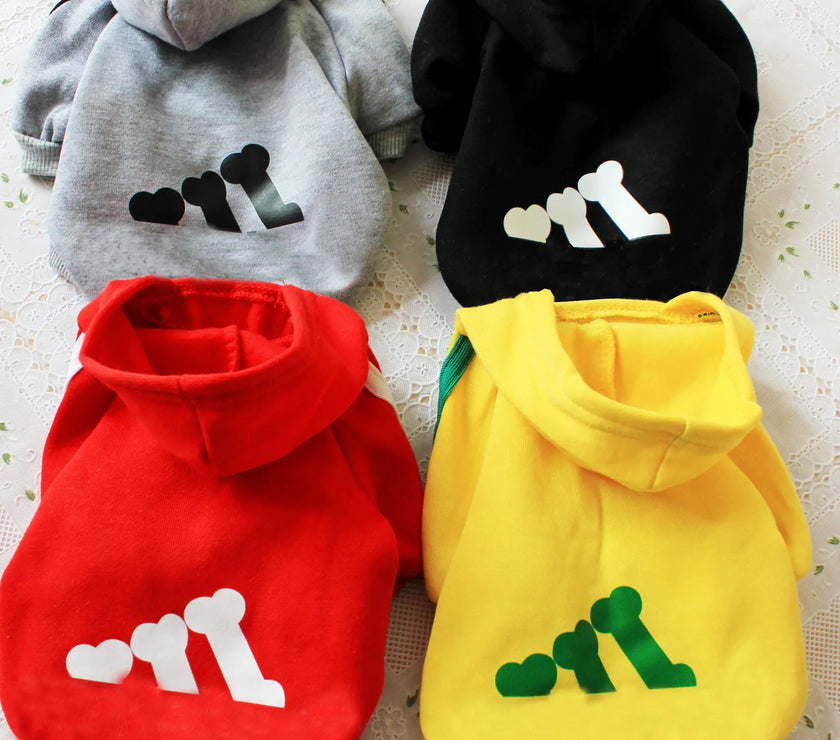 Four pet hoodies in gray, black, red, and yellow with paw print designs on a textured surface.