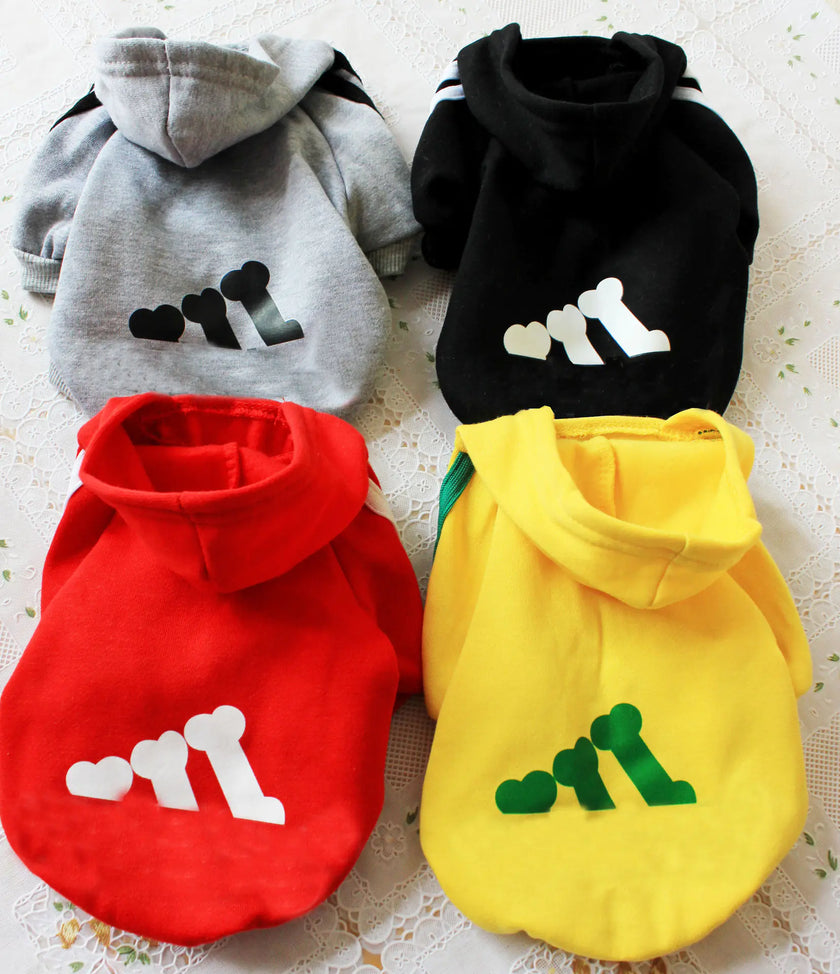 Four pet hoodies in gray, black, red, and yellow with paw print designs on a textured surface.