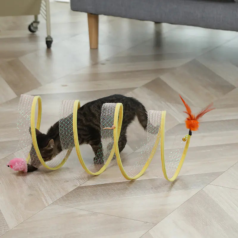 Cat playing with a yellow mesh tunnel toy on a wooden floor.